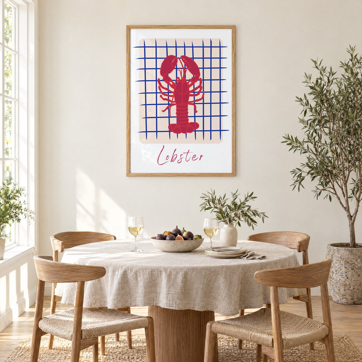 Lobster on cobalt grid print in an oak frame above a round linen-covered dining table with figs and wine