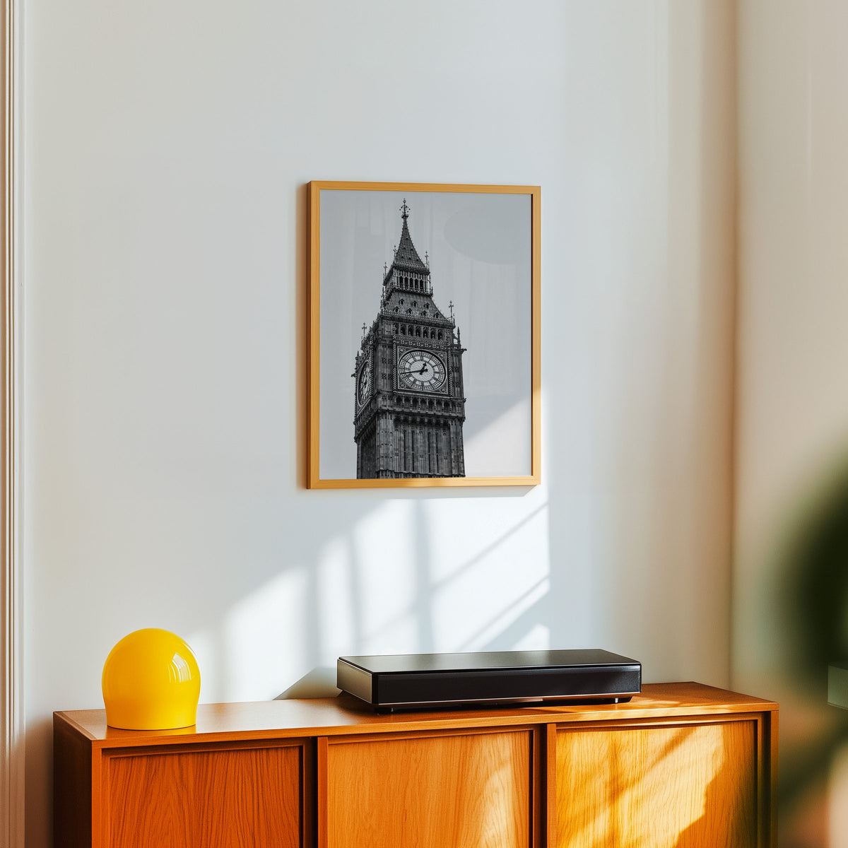 Big Ben clock tower low-angle photo print in an oak frame above a teak sideboard with a yellow glass lamp