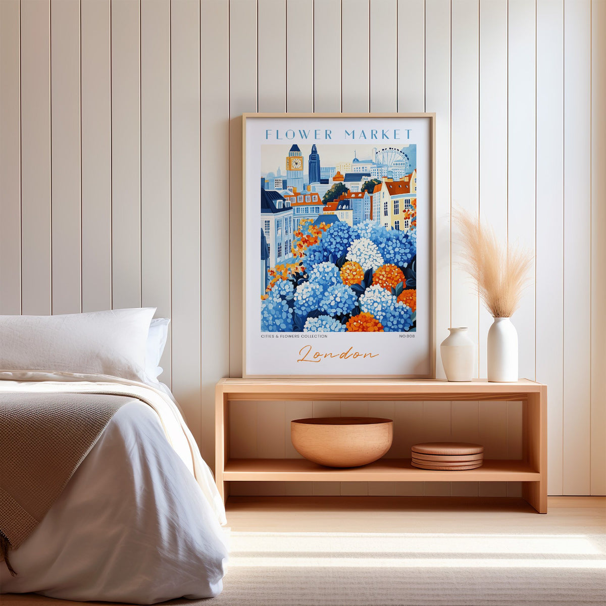 London flower market print in an oak frame on a wood bench against a white shiplap bedroom wall with pampas grass