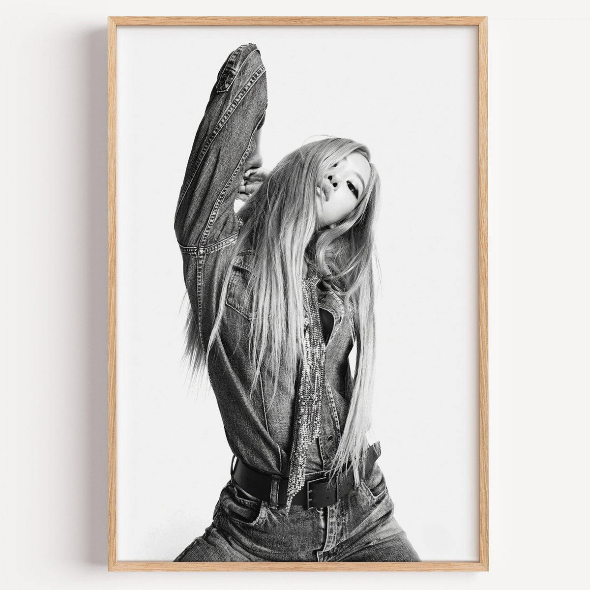 Model in oversized denim jacket, arm raised print in a light oak frame on a plain white wall