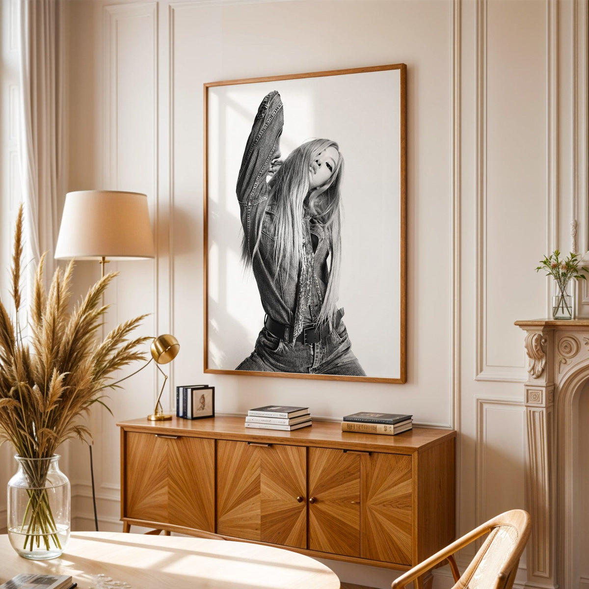 Model in oversized denim jacket, arm raised print in an oak frame above a sunburst wood sideboard with pampas grass