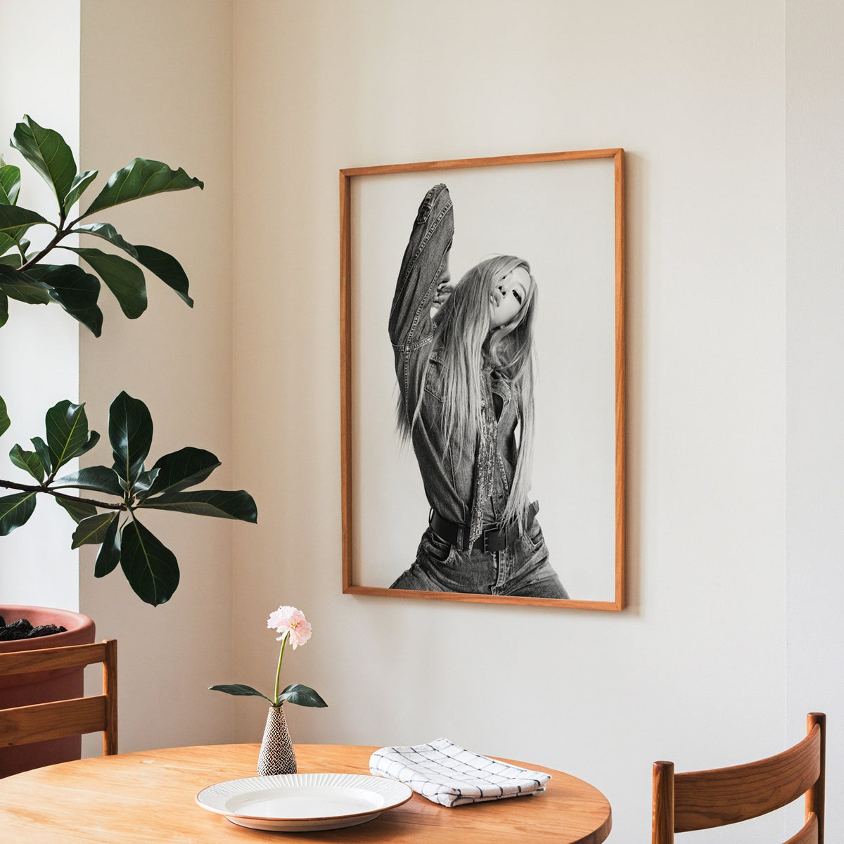 Model in oversized denim jacket, arm raised print in a teak frame above a round wooden dining table