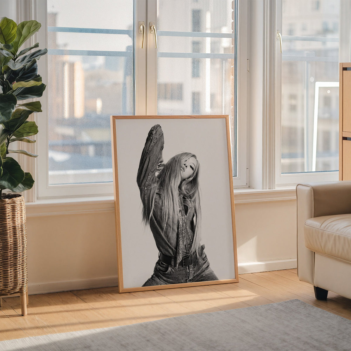 Model in oversized denim jacket, arm raised print in an oak frame leaning on the floor beside a fiddle leaf fig