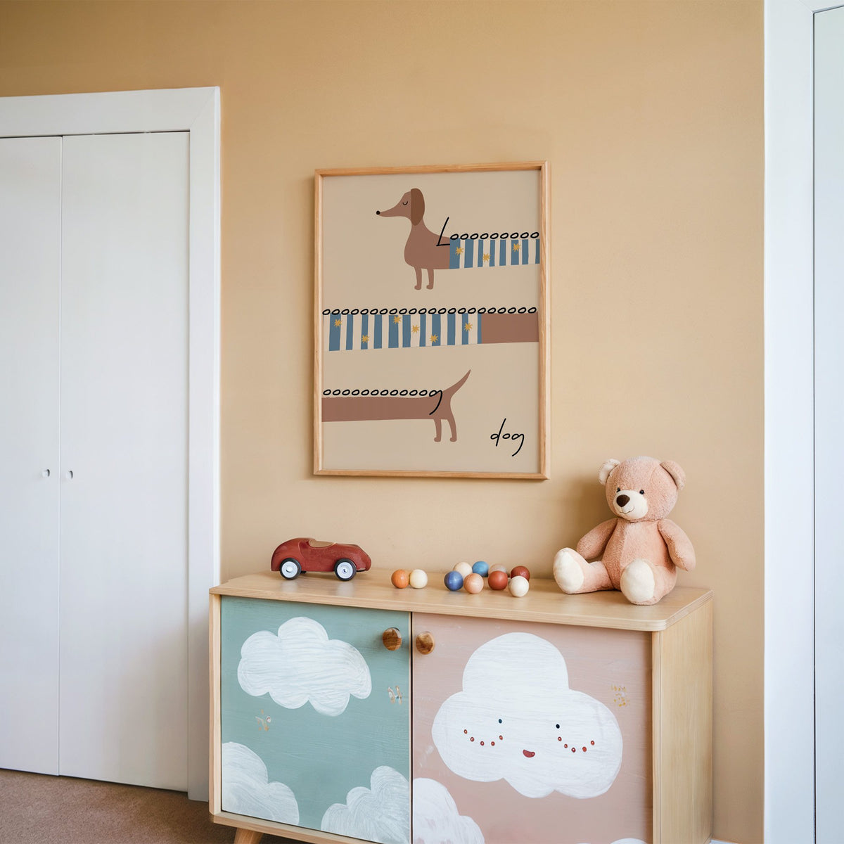 Long dog dachshund sweater nursery print in an oak frame on a peach wall above a cloud-painted cabinet