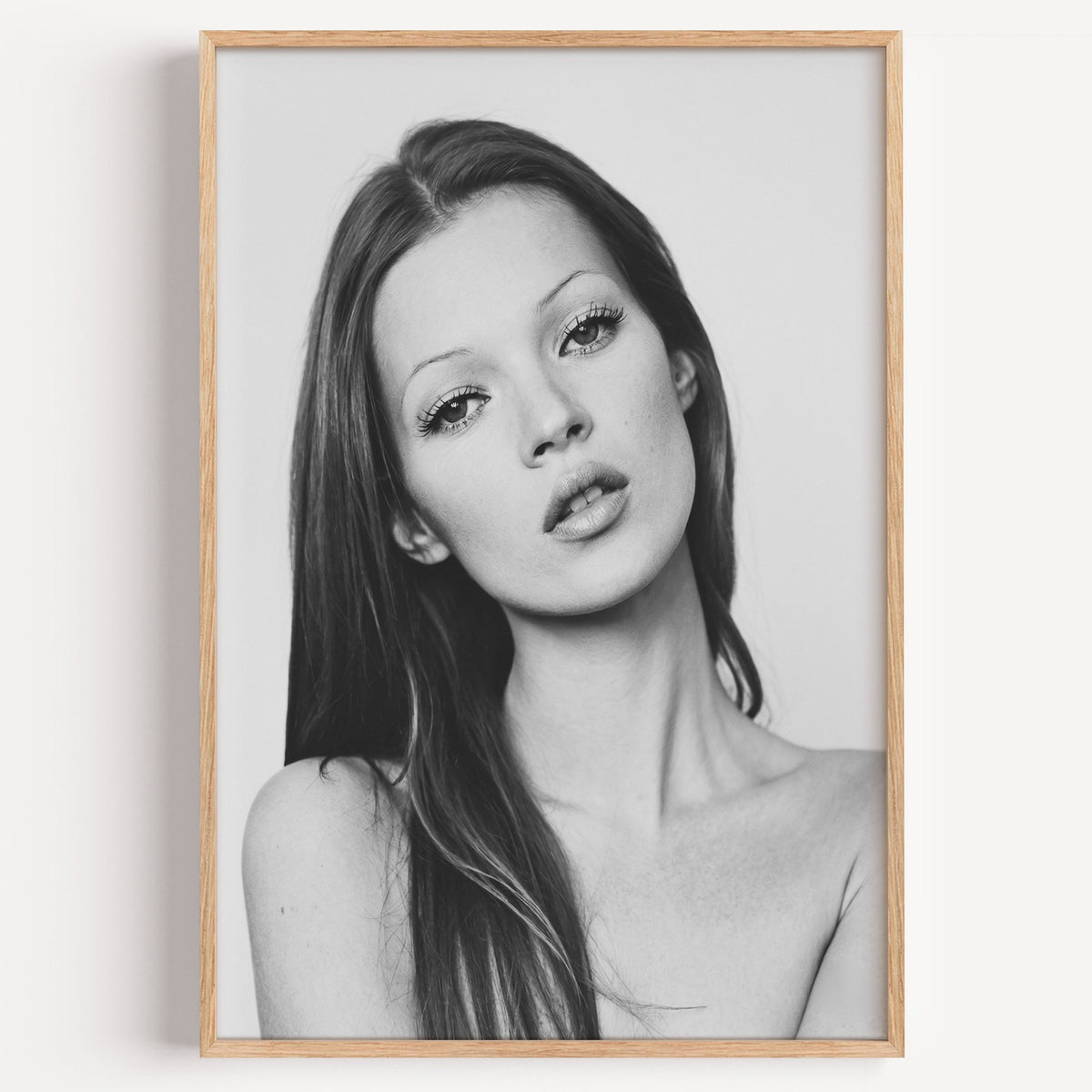 Woman with long dark hair tilting her head print in a light oak frame on a plain white wall