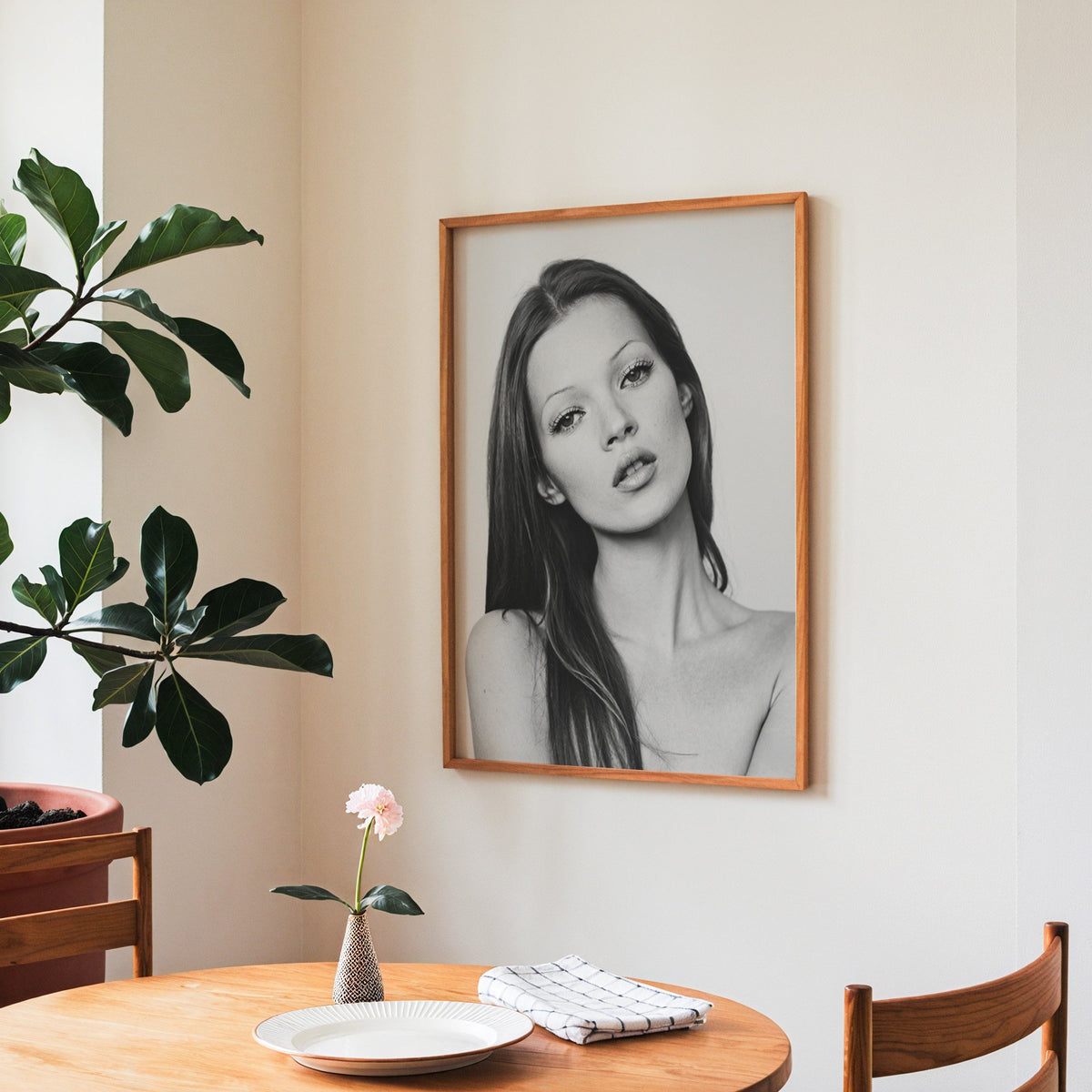 Woman with long dark hair tilting her head print in a teak frame above a round wooden dining table