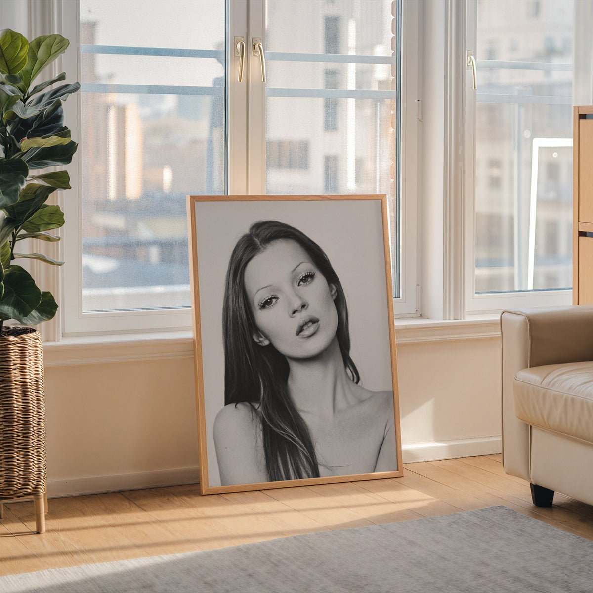 Woman with long dark hair tilting her head print in an oak frame leaning on the floor beside a fiddle leaf fig