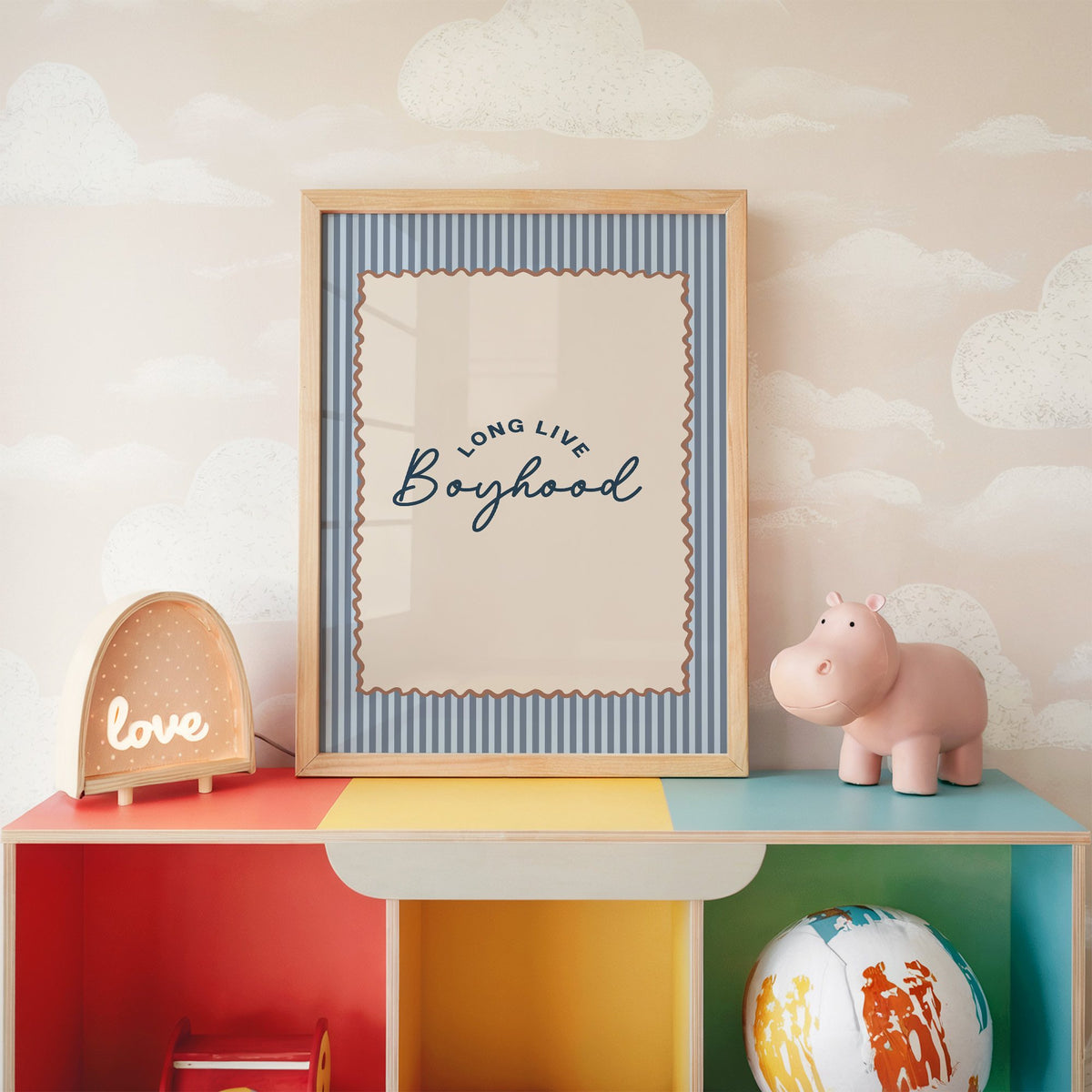 Long live boyhood nursery print in an oak frame on a rainbow toy shelf against cloud wallpaper