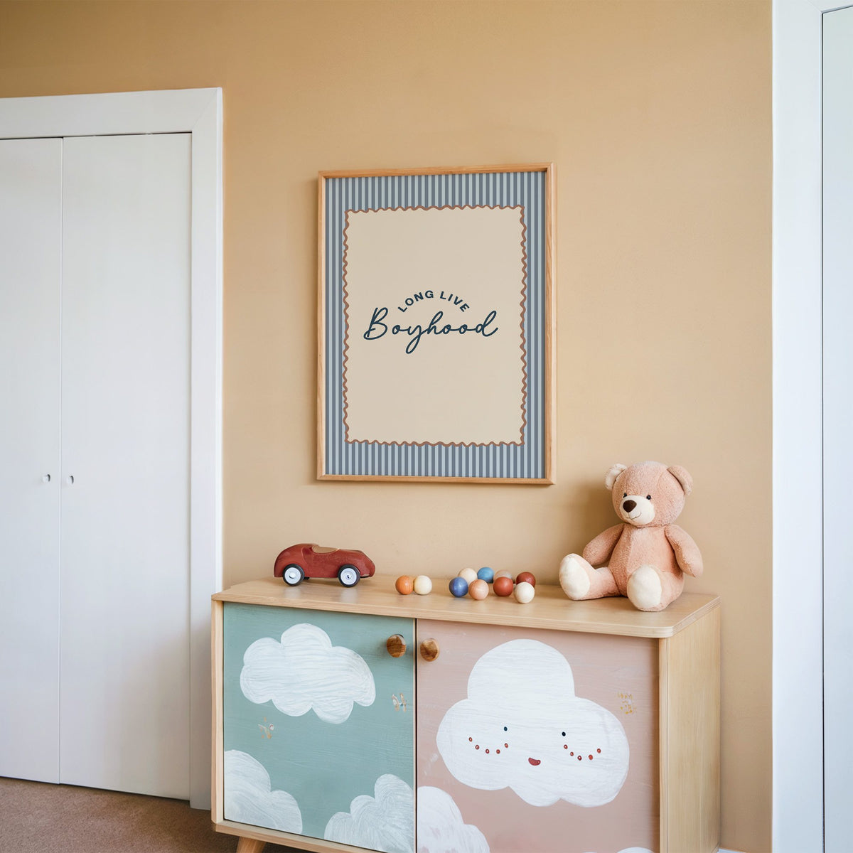 Long live boyhood nursery print in an oak frame on a peach wall above a cloud-painted cabinet