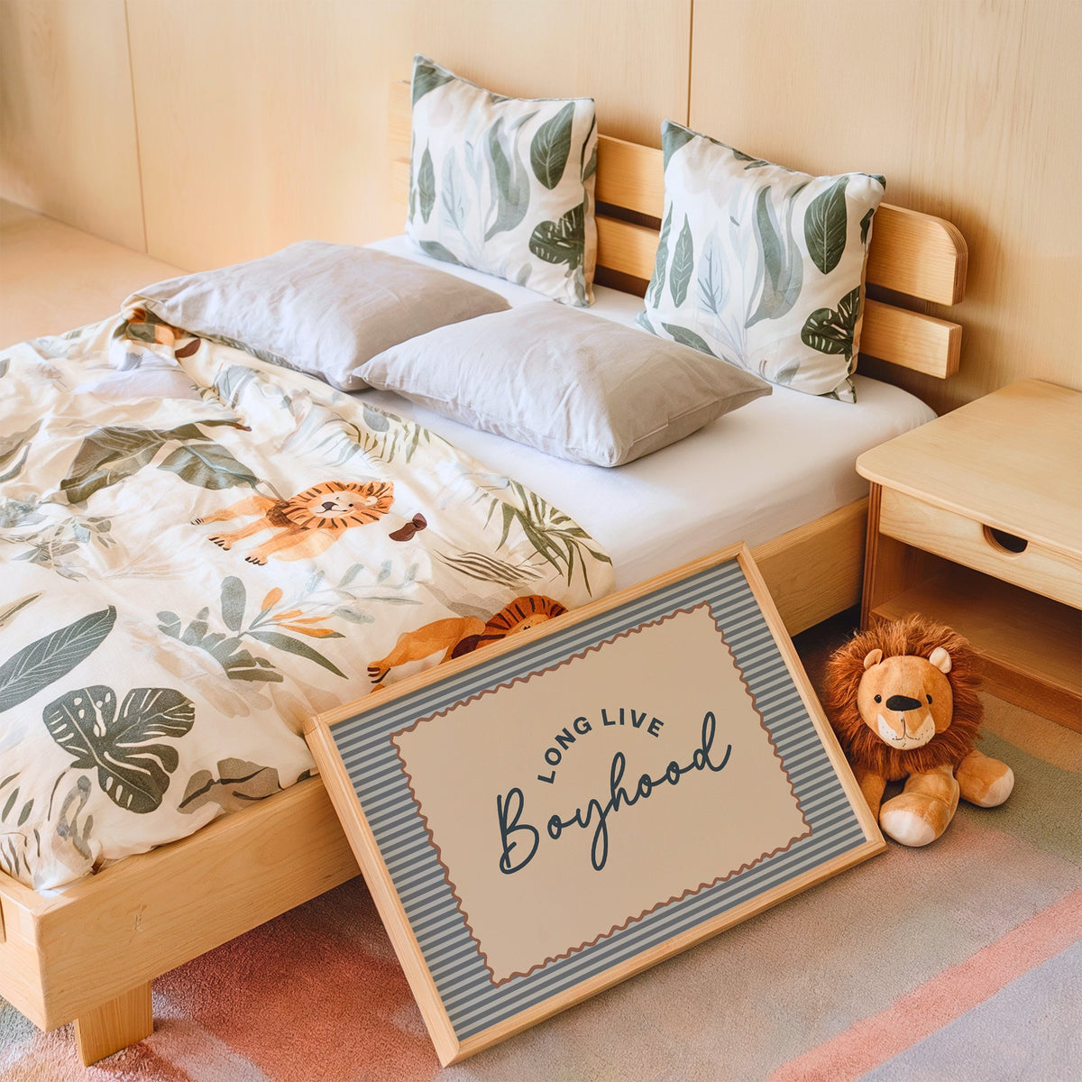 Landscape long live boyhood nursery print in an oak frame leaning on a kids bed by a lion plush