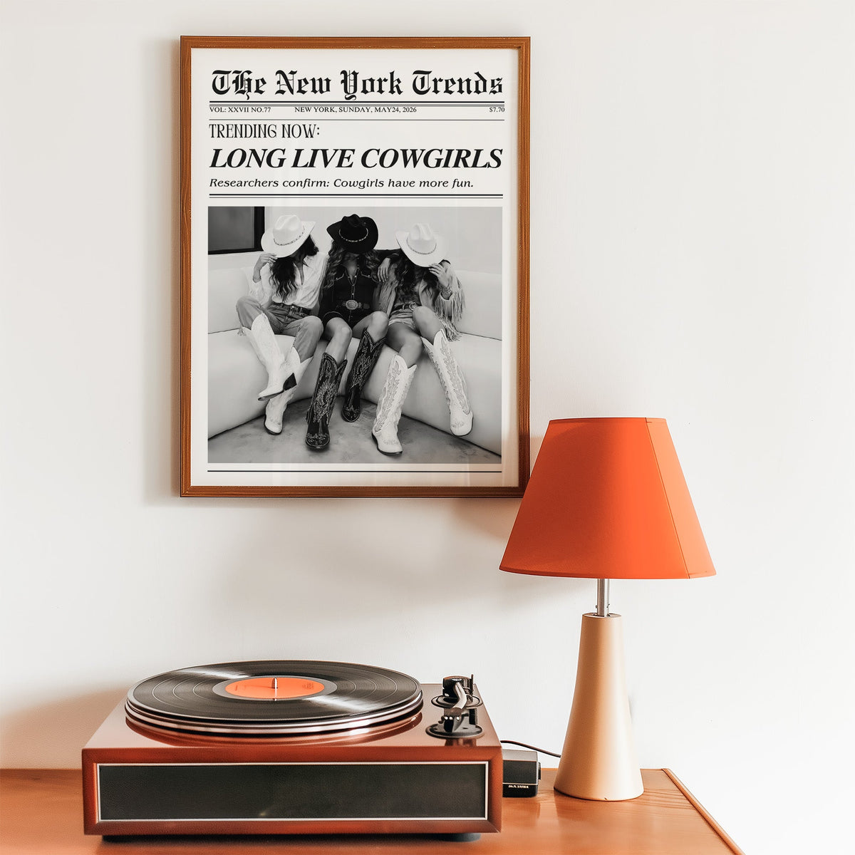 Three cowgirls on white sofa mock newspaper print in a walnut frame above a record player and orange lamp