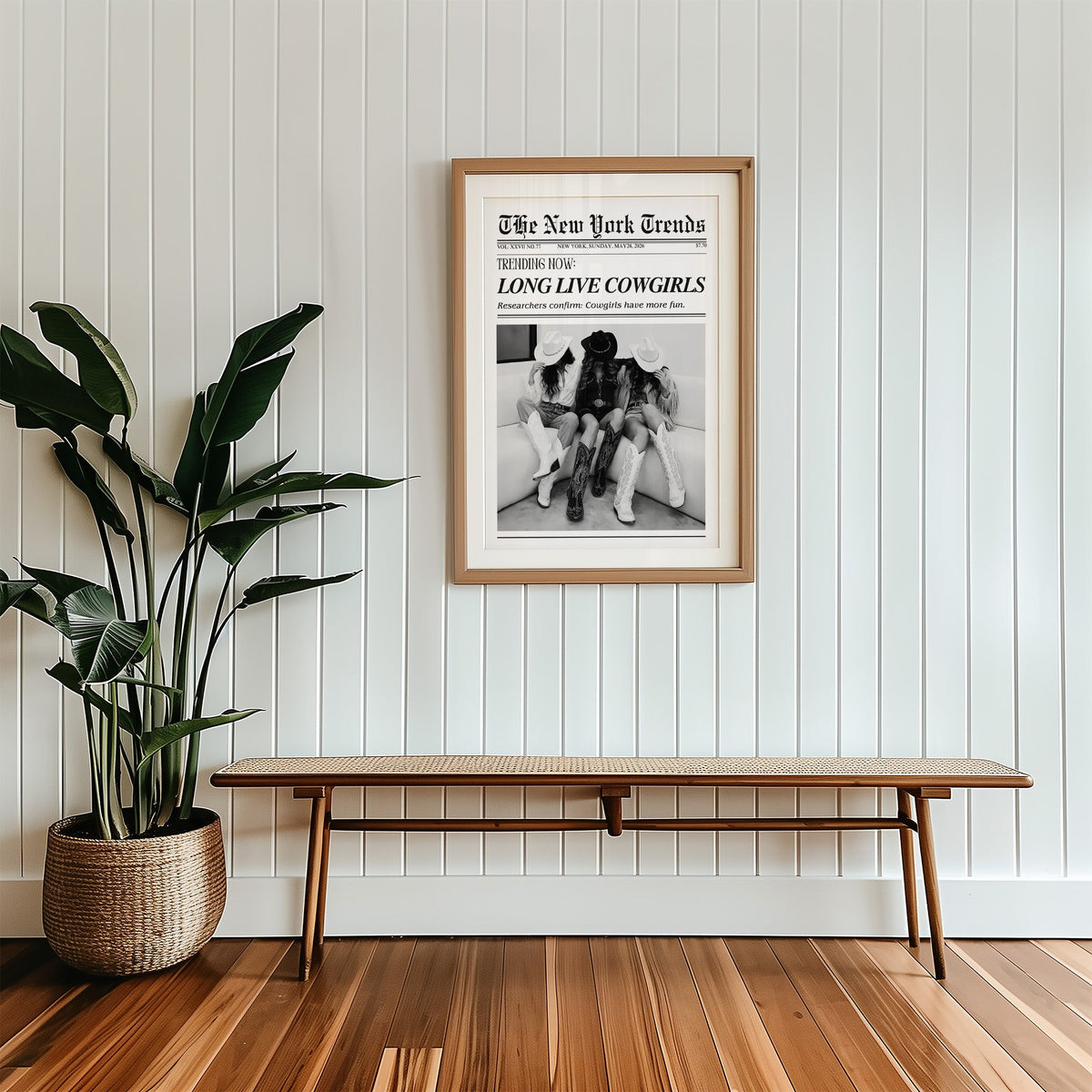 Three cowgirls on white sofa mock newspaper print in a wood frame with a white mat above a cane bench