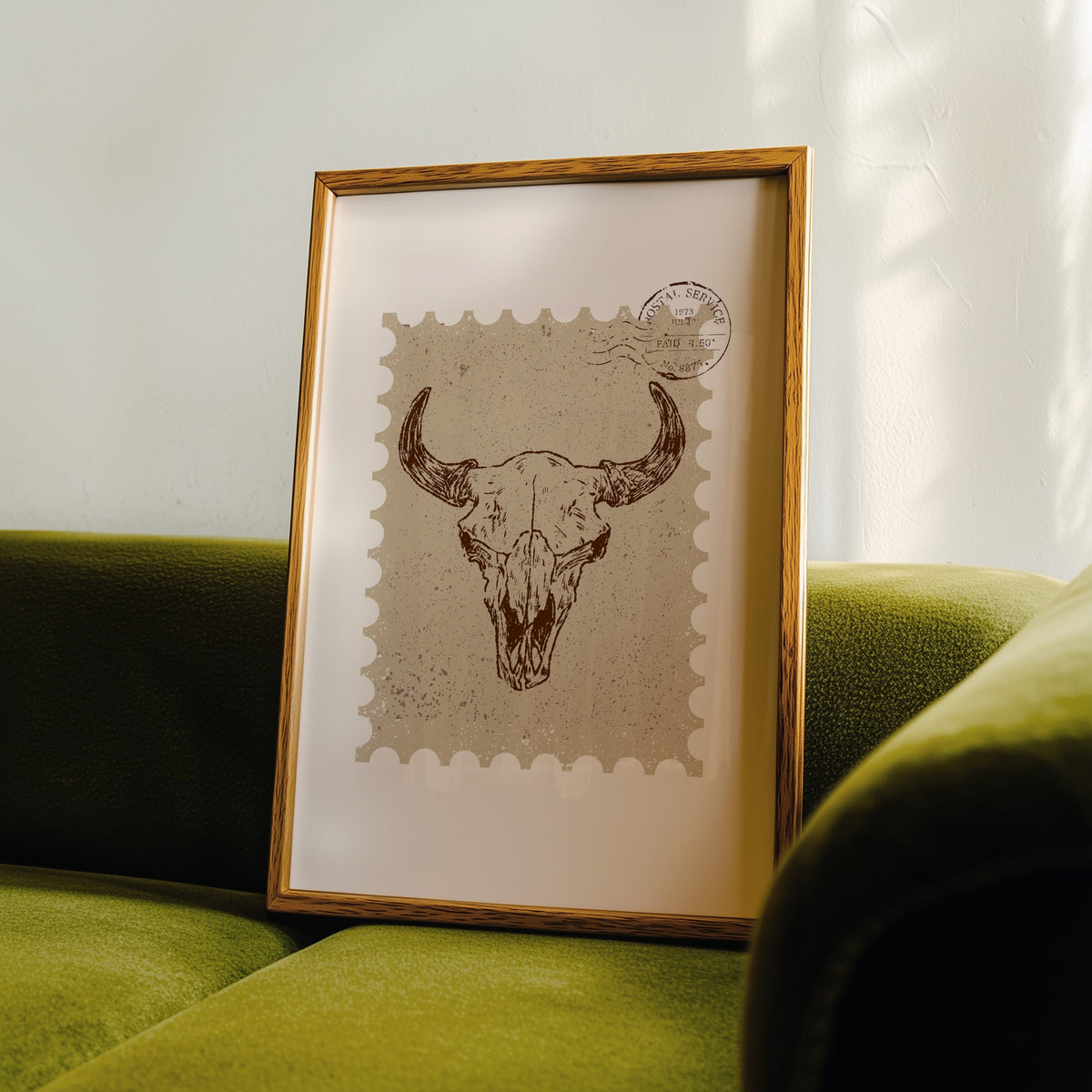Longhorn skull stamp print in an oak frame leaning on a green velvet sofa