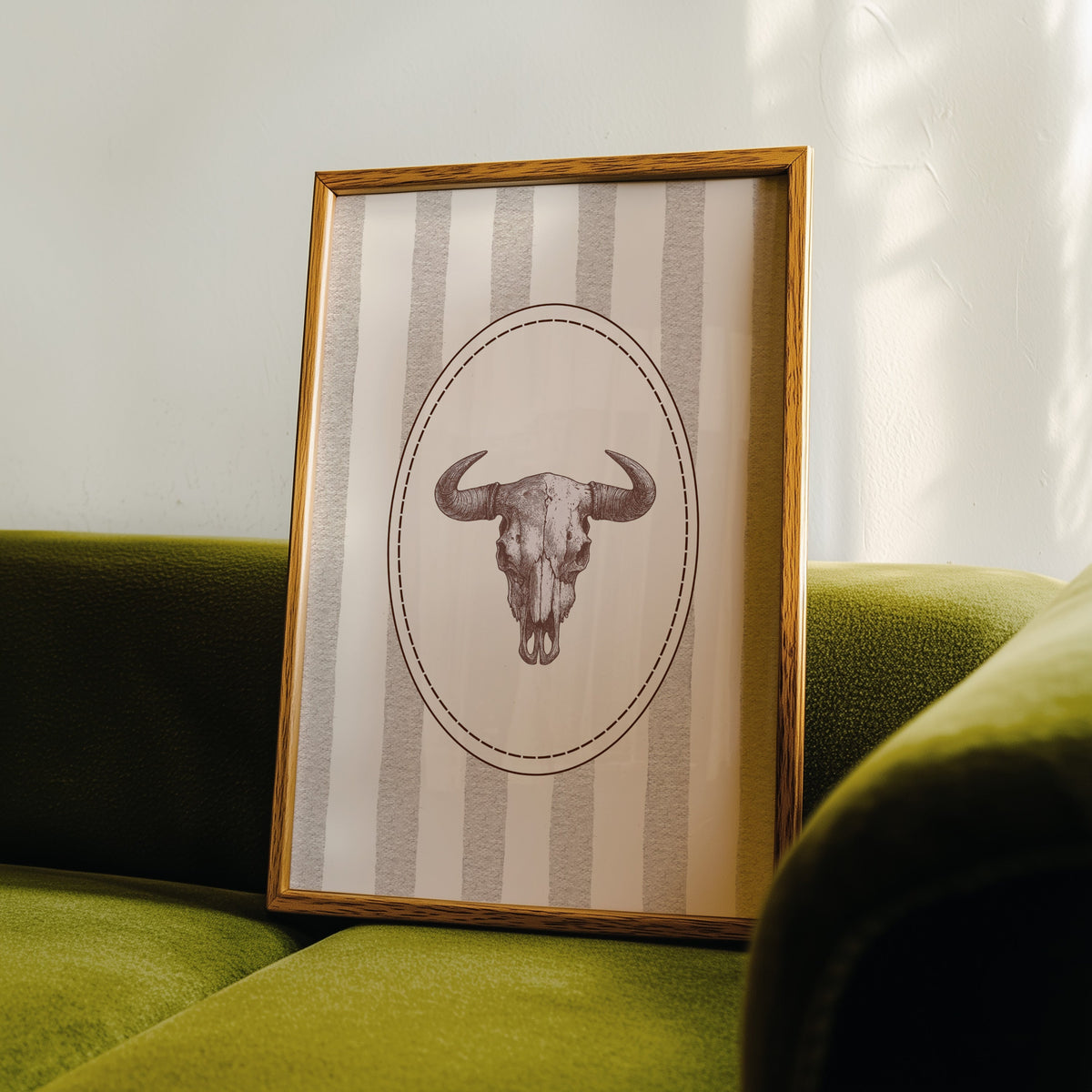 Longhorn skull cameo print in an oak frame leaning on a green velvet sofa