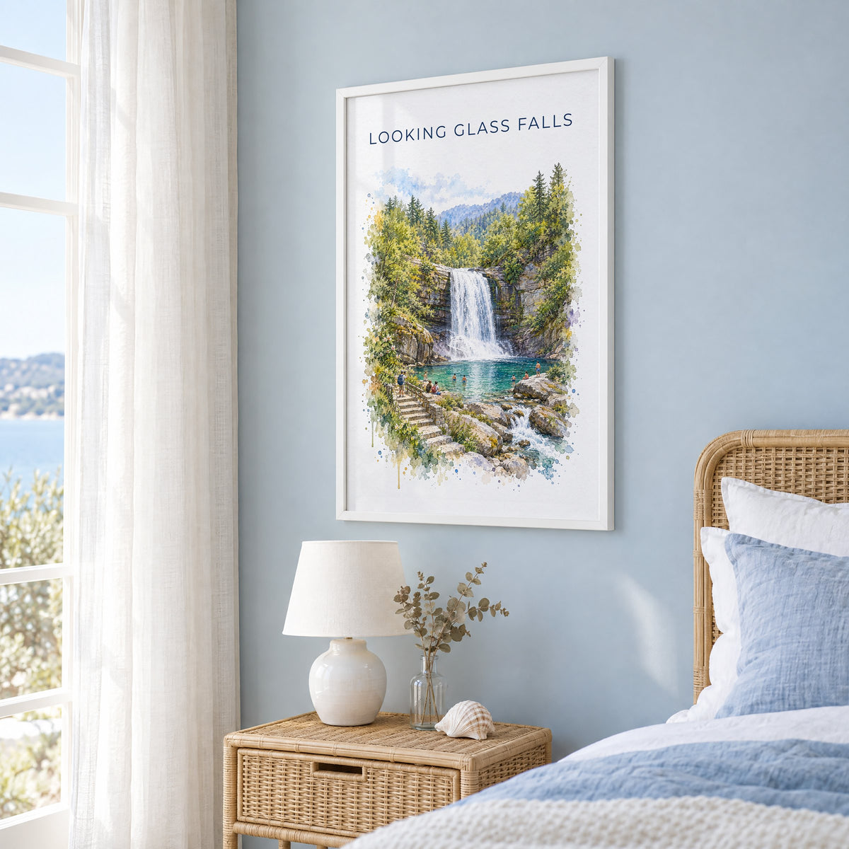 Looking Glass Falls watercolor print in a white frame on a pale blue wall beside a rattan bed in a coastal bedroom
