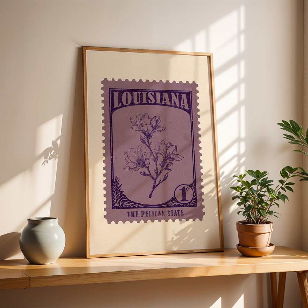 Louisiana Magnolia stamp print in a light oak frame leaning on a wooden table beside a stoneware vase