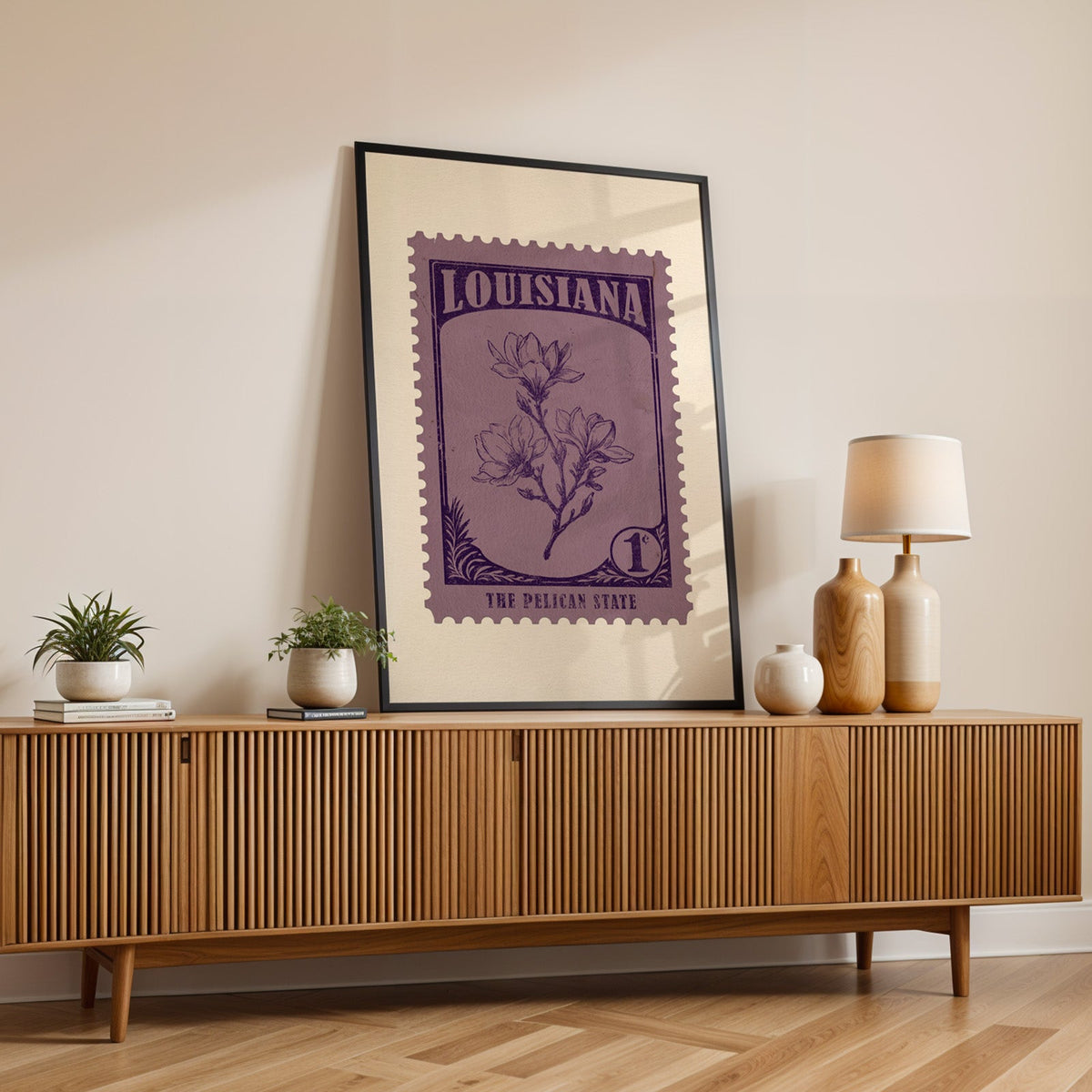 Louisiana state flower print in a black frame leaning on a fluted wood credenza with vases and a lamp