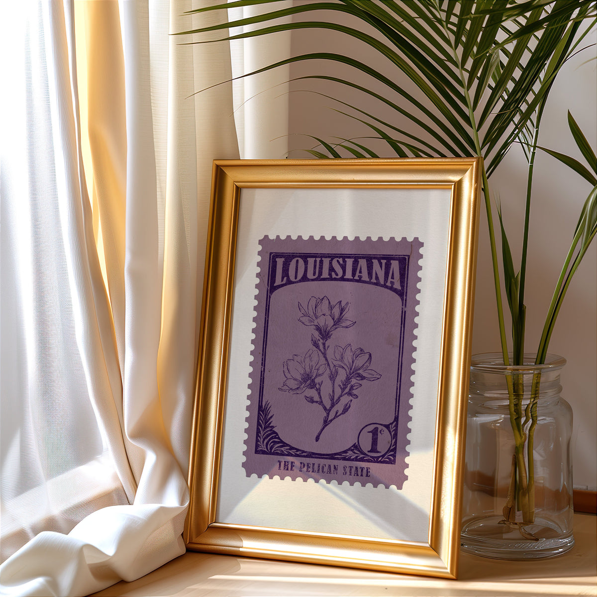 Louisiana stamp print in a gold frame leaning by a cream curtain with a palm in a glass jar
