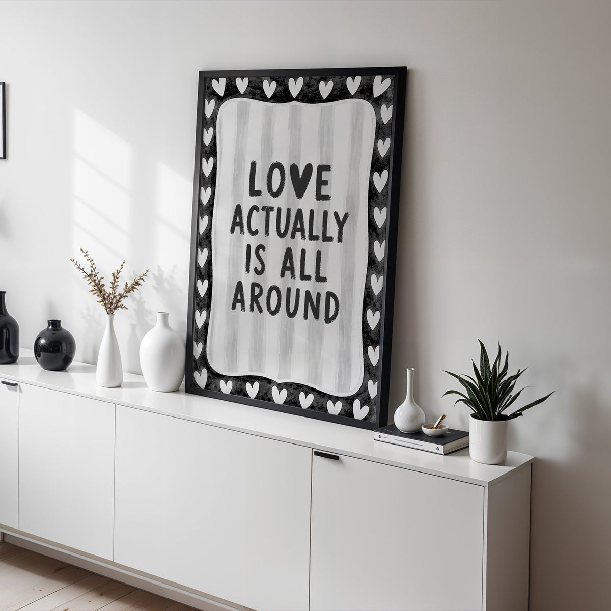 Love actually is all around hearts border print in a black frame on a white sideboard with black and white vases