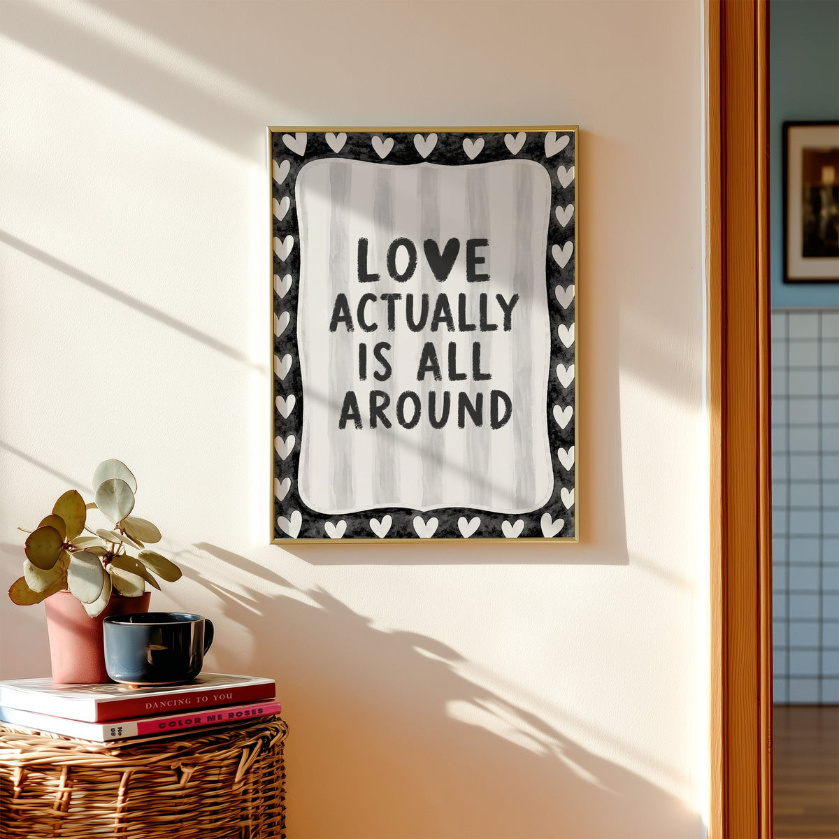 Love actually is all around hearts border print shown in a gold frame above a wicker basket and stacked books