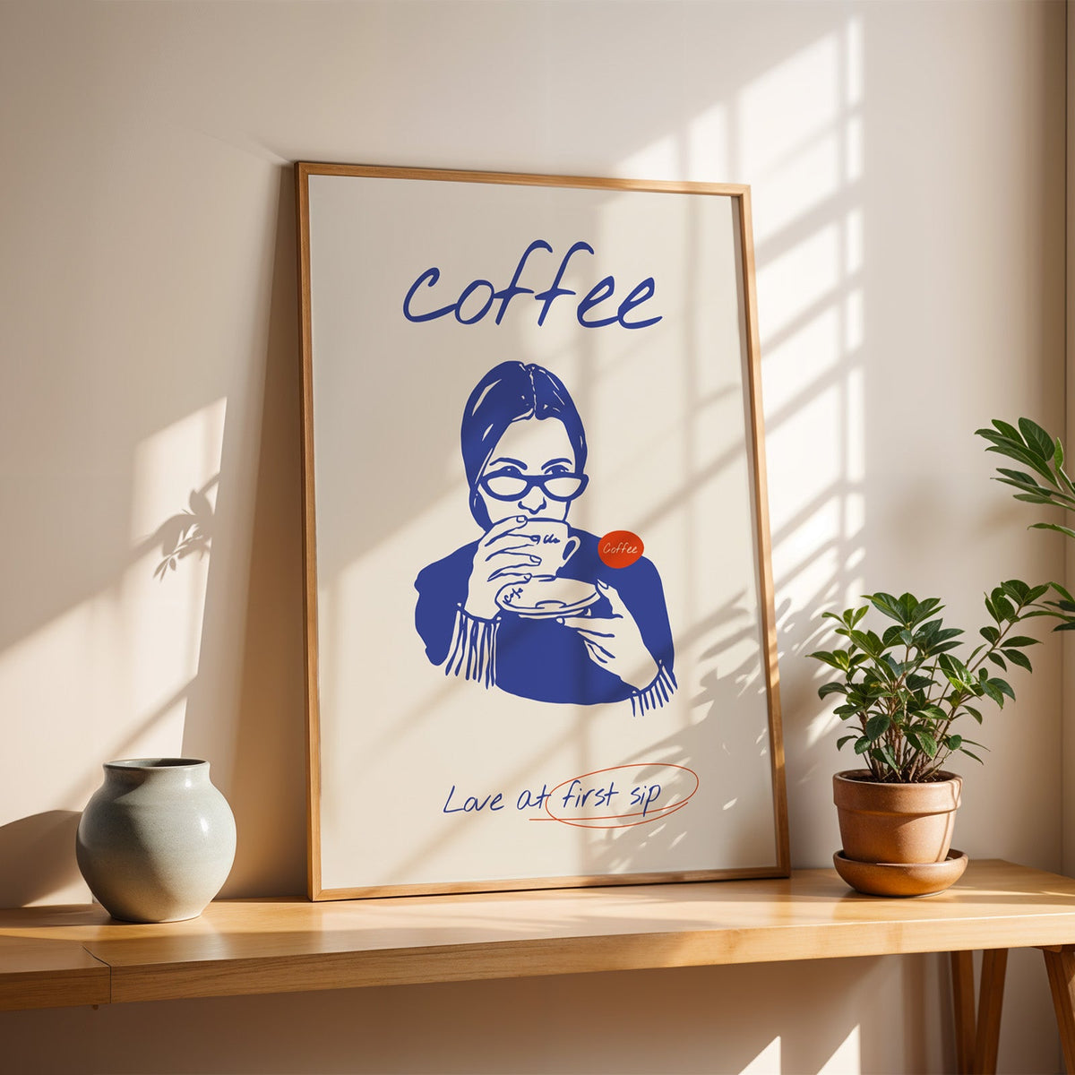 Love at First Sip poster in a slim oak frame on a sunlit wood console with a stoneware vase