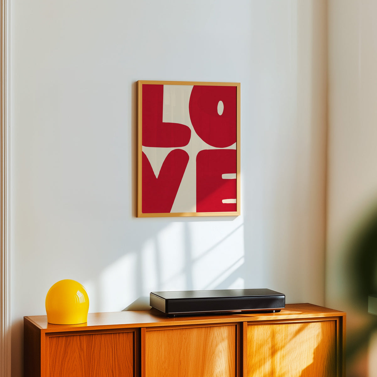 LOVE word art print in a light oak frame above a teak sideboard with a yellow lamp
