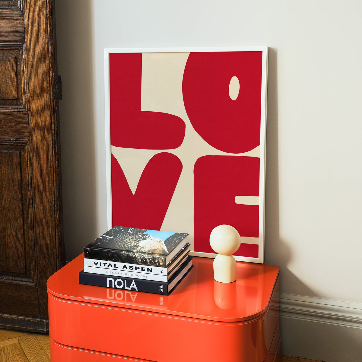 Red LOVE typography print in a white frame on a glossy orange cabinet with books