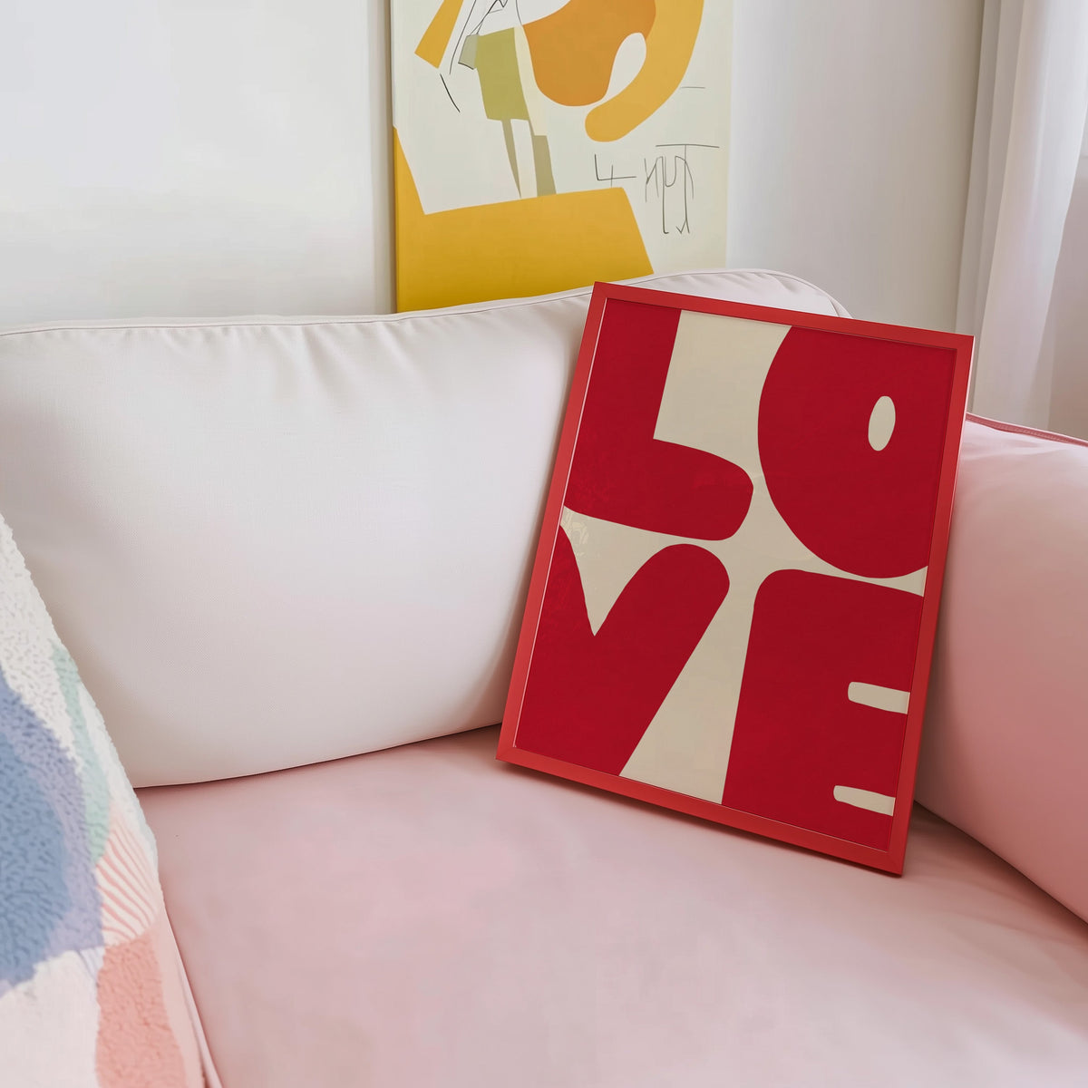 Bold red letters print shown in a red frame leaning on a blush pink sofa