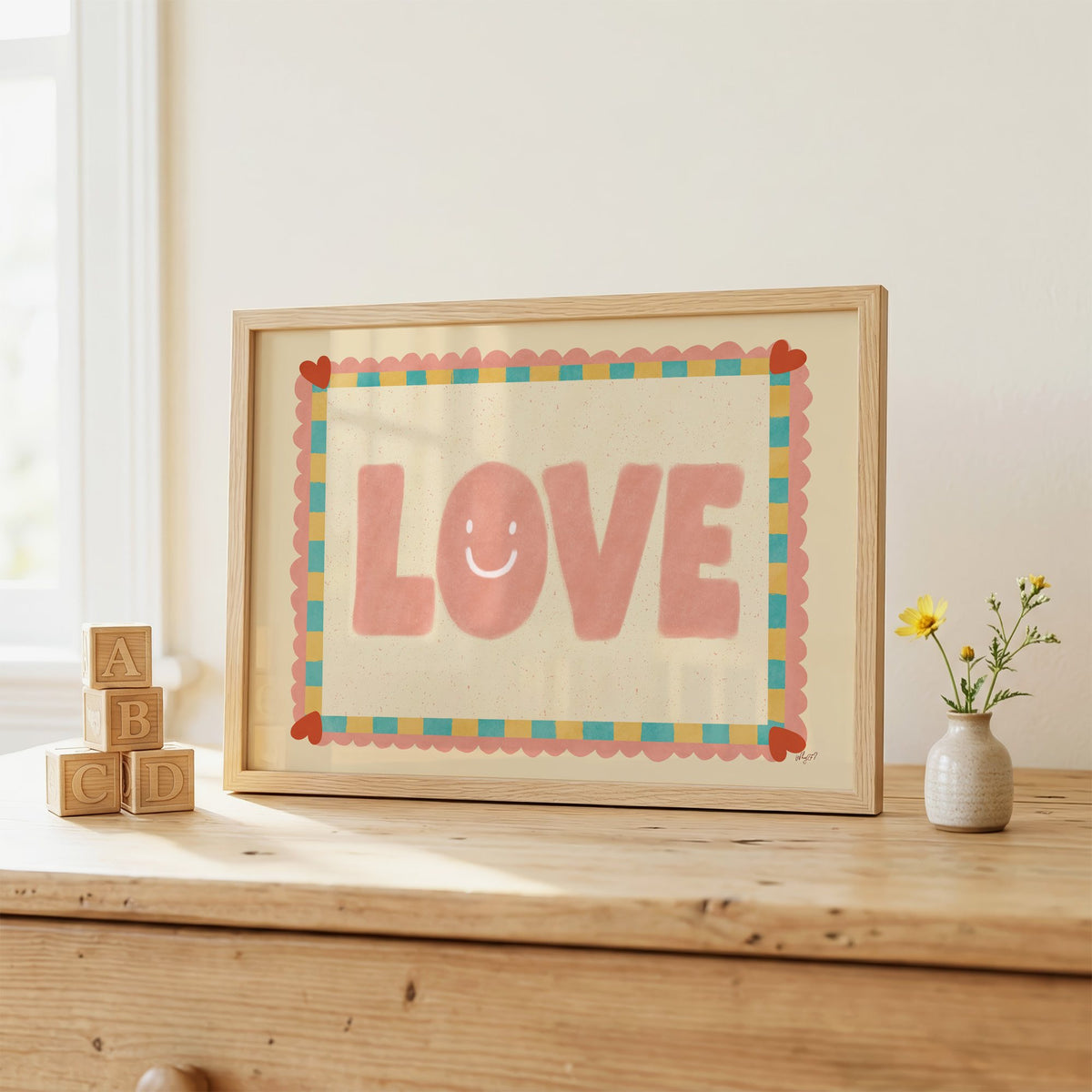 Love smiley face checkered border nursery print in an oak frame on a wooden dresser beside ABC blocks