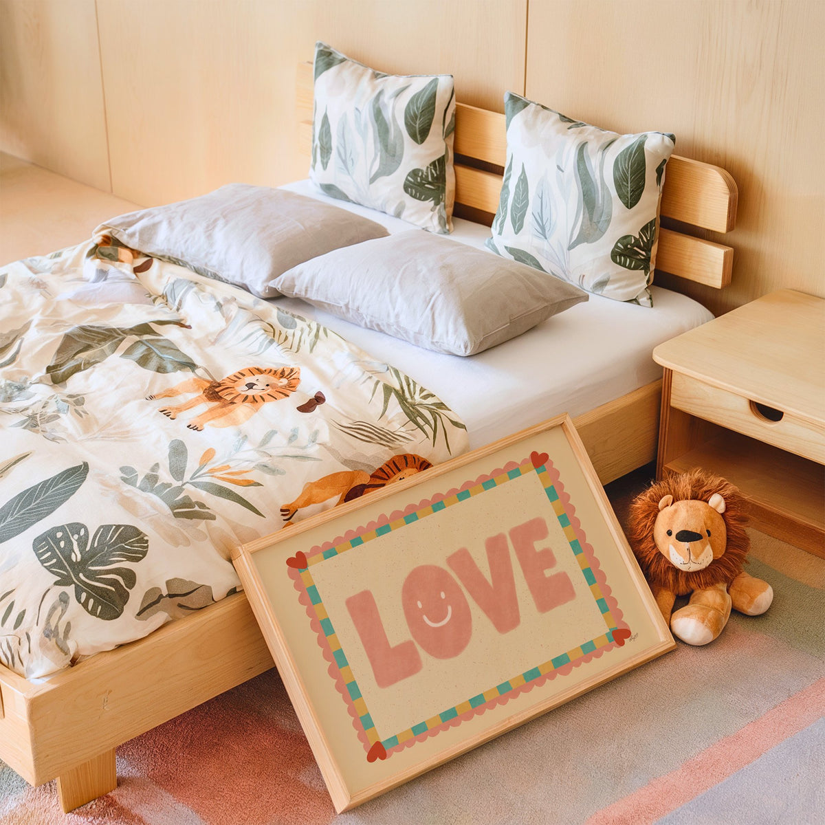 Love smiley face checkered border nursery print in an oak frame leaning on a kids bed by a lion plush