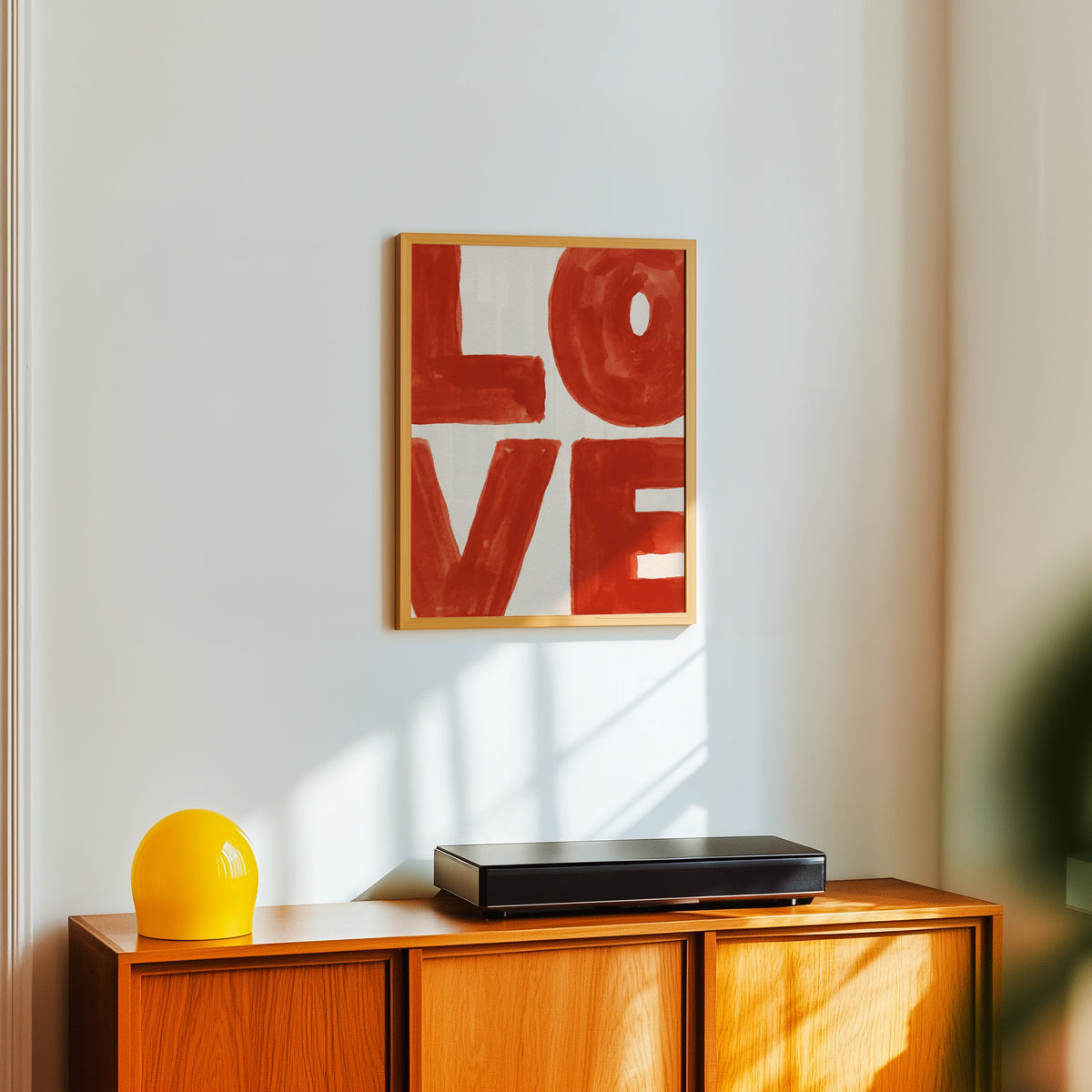 LOVE typography print in a light oak frame above a teak sideboard with a yellow lamp