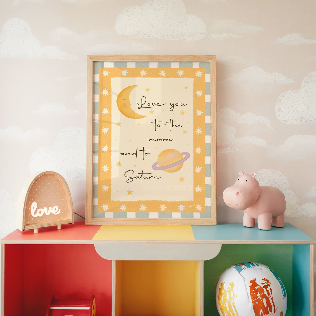 Love you moon and saturn nursery print in an oak frame on a rainbow toy shelf against cloud wallpaper