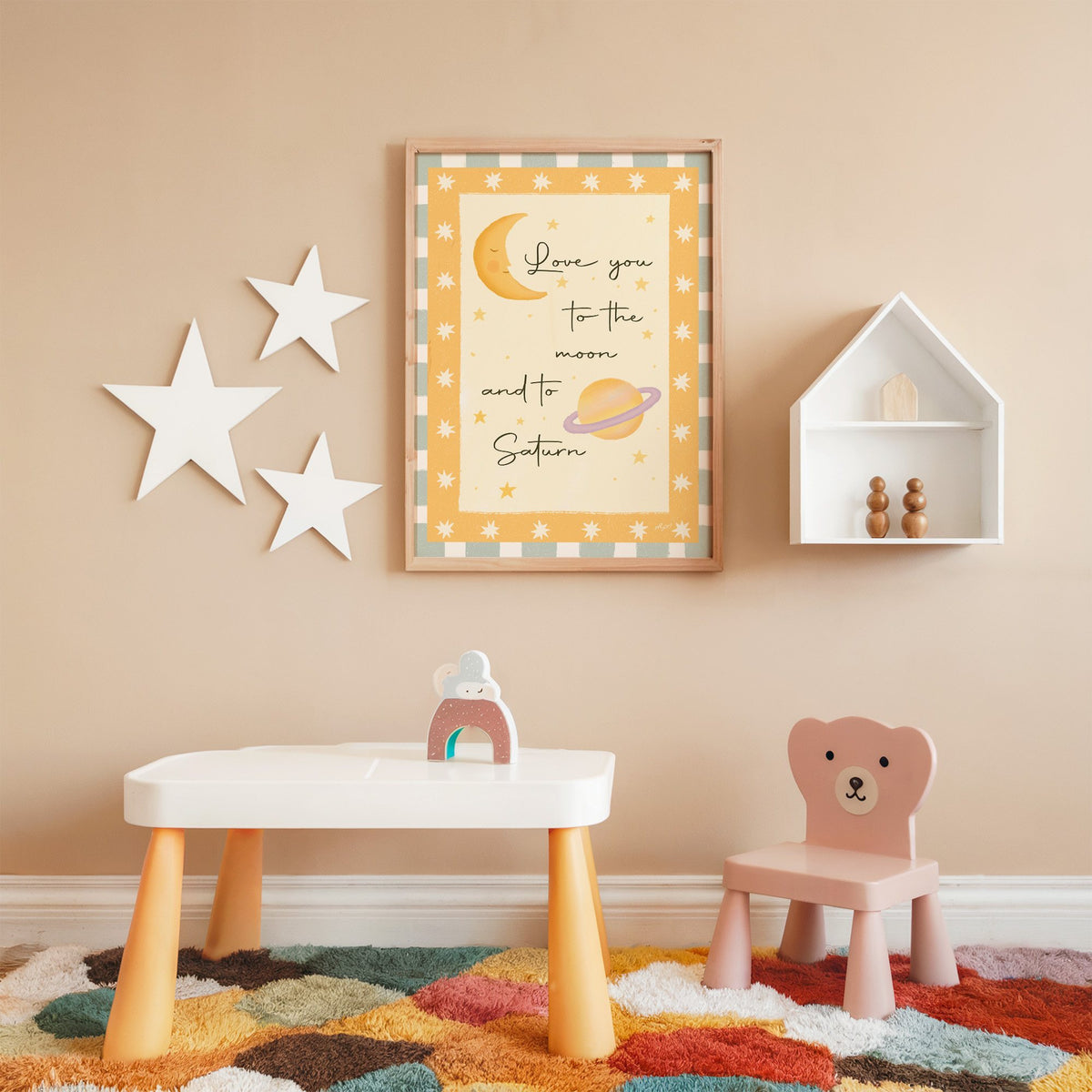 Love you moon and saturn nursery print in an oak frame on a peach wall above a kids table with wall stars