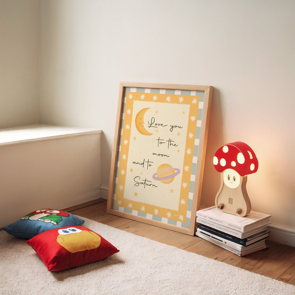 Love you moon and saturn nursery print in an oak frame leaning on a rug beside a mushroom lamp and floor cushions