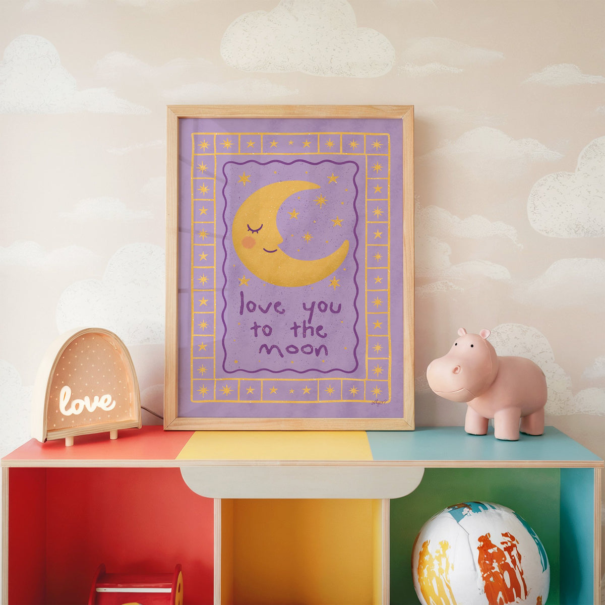 Lavender love you to the moon nursery print in an oak frame on a rainbow toy shelf against cloud wallpaper