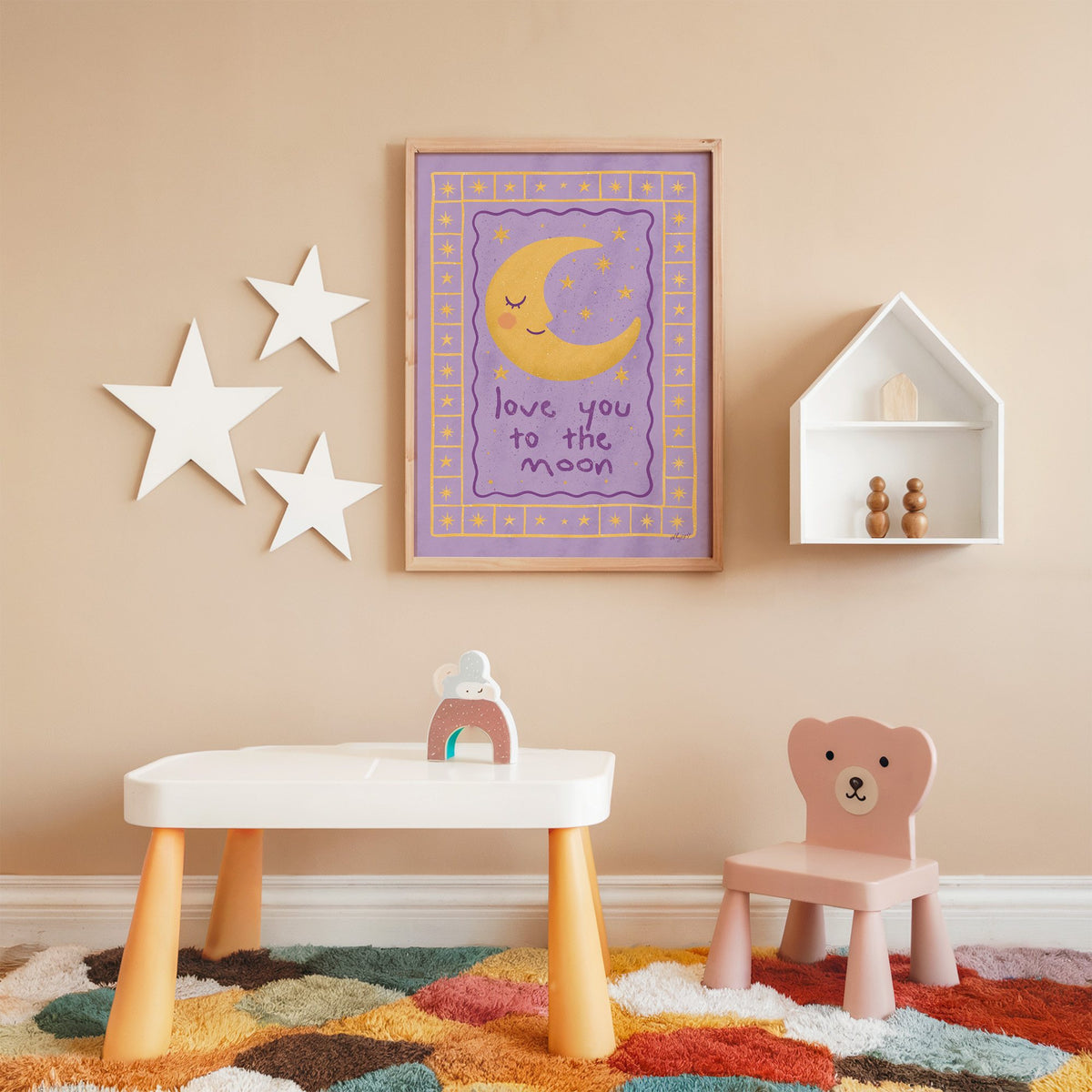 Lavender love you to the moon nursery print in an oak frame on a peach wall above a kids table with wall stars