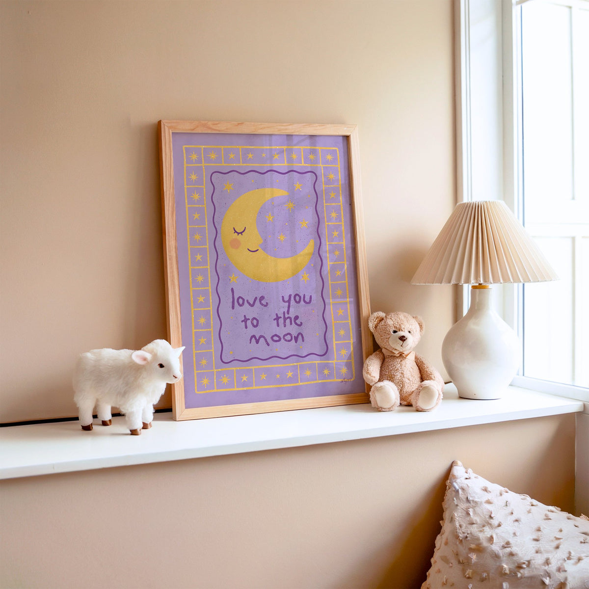 Lavender love you to the moon nursery print in an oak frame on a window ledge with a toy lamb and teddy