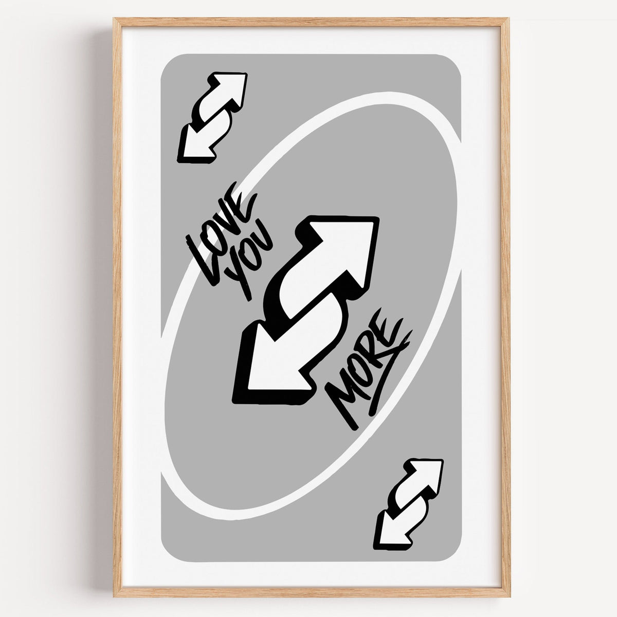 Love you more reverse arrows card print in a light oak frame on a plain white wall