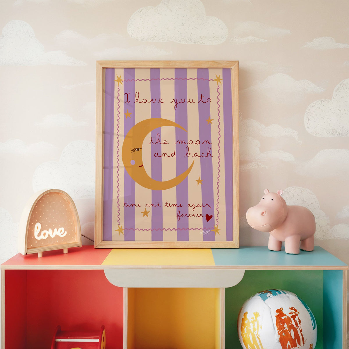 Love you to the moon lilac nursery print in an oak frame on a rainbow toy shelf against cloud wallpaper