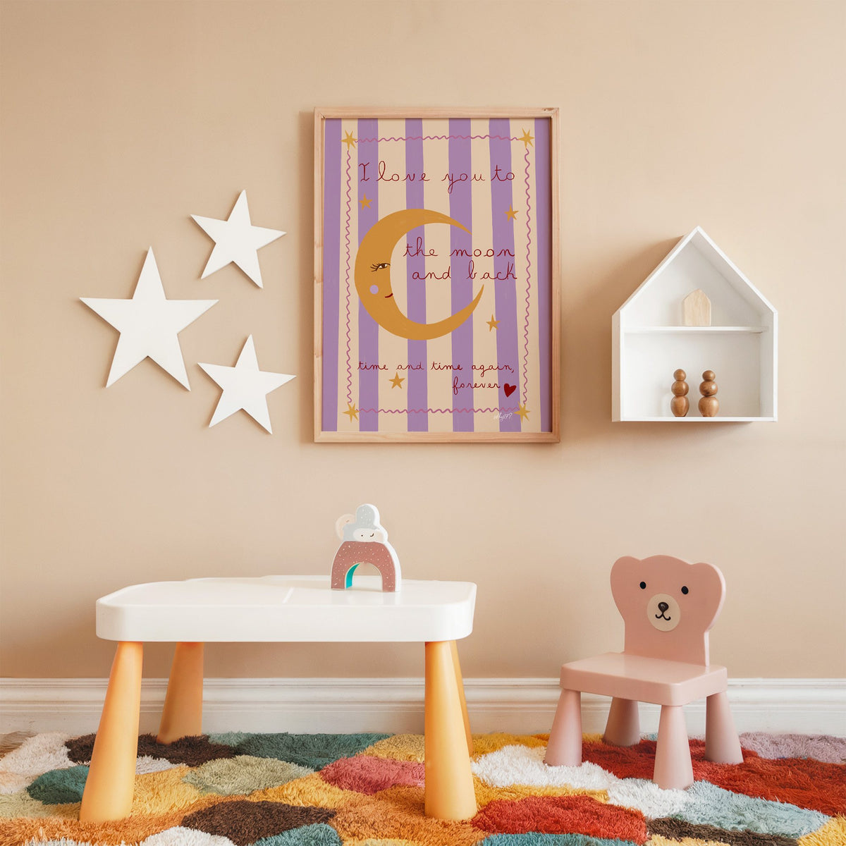 Love you to the moon lilac nursery print in an oak frame on a peach wall above a kids table with wall stars