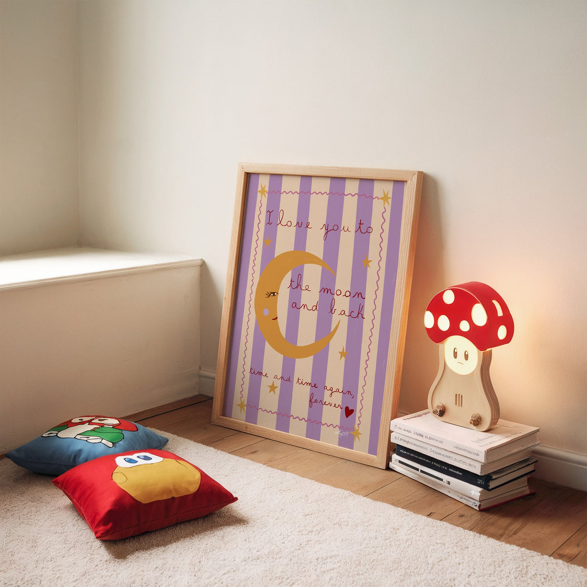 Love you to the moon lilac nursery print in an oak frame leaning on a rug beside a mushroom lamp and floor cushions
