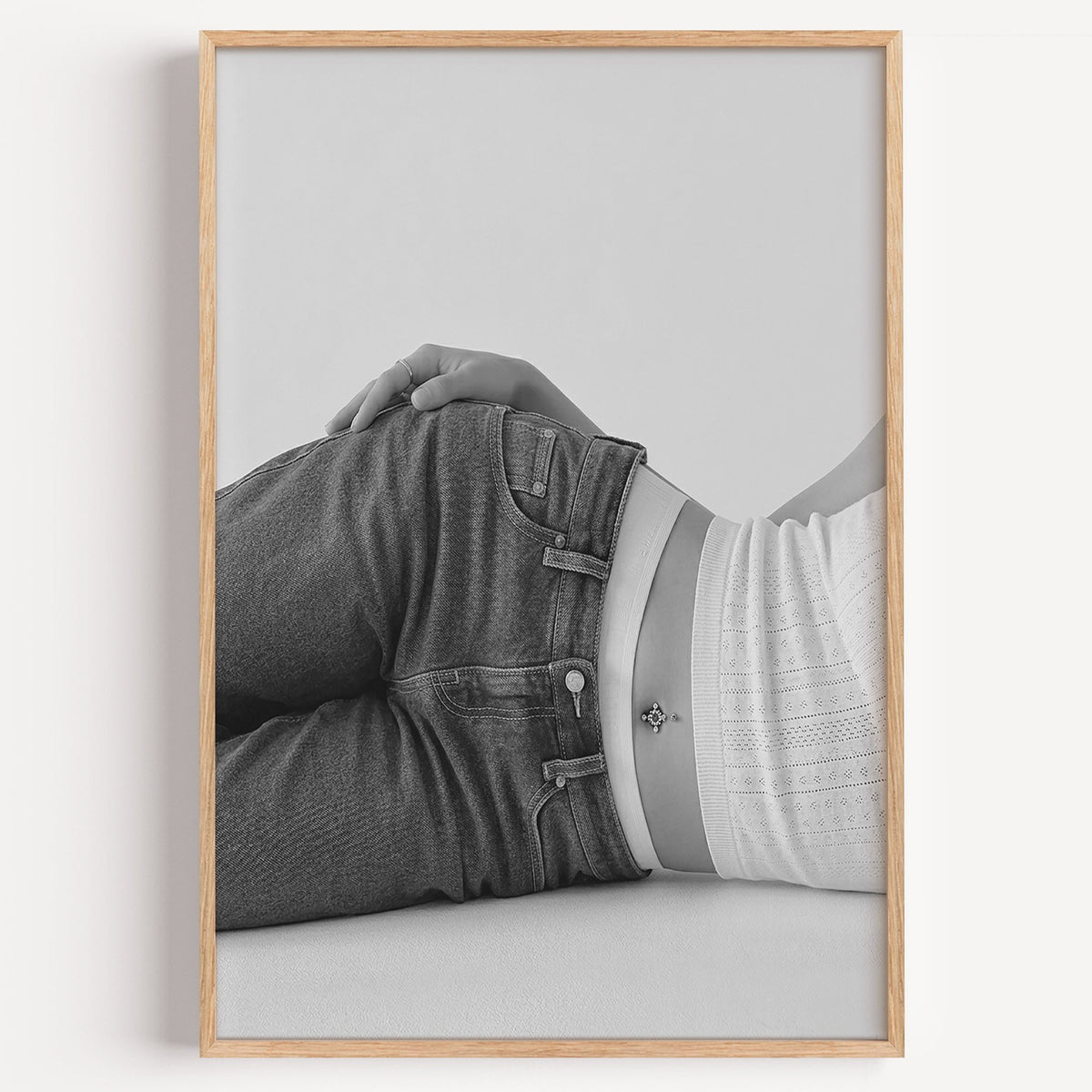 Woman lying in low rise jeans on grey print in a light oak frame on a plain white wall
