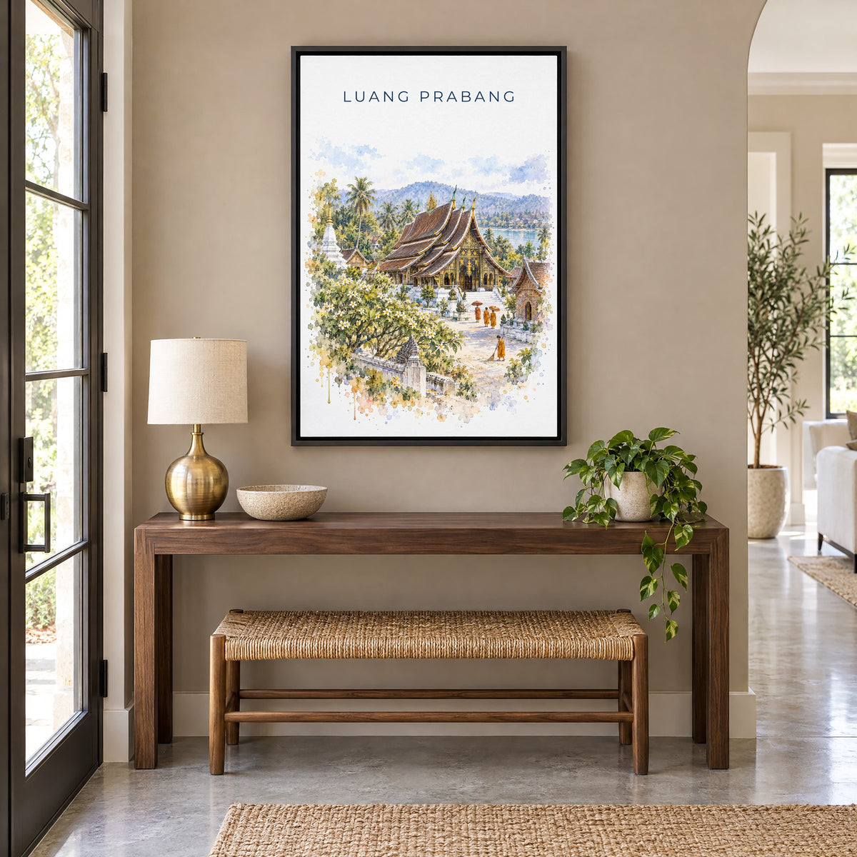 Luang Prabang watercolor print as a black floater canvas above a walnut console and woven bench in an entryway