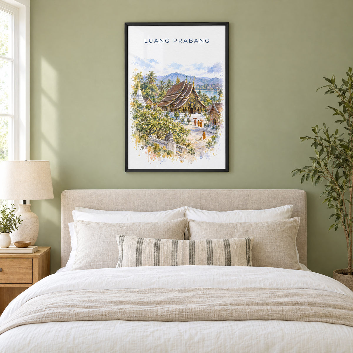 Luang Prabang watercolor print in a black frame above an upholstered headboard in a sage green bedroom
