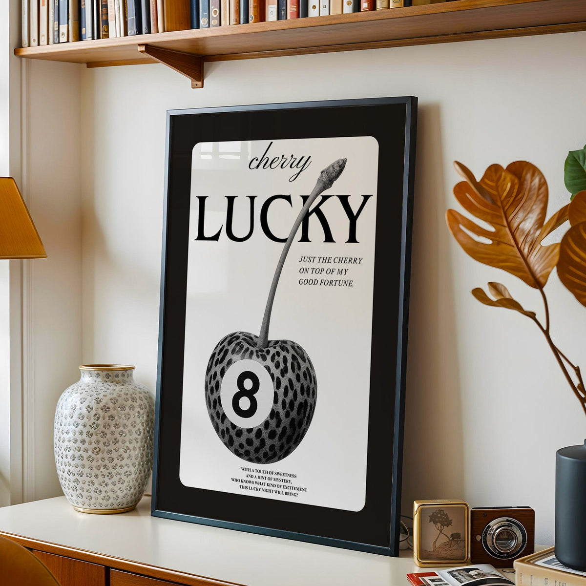 Leopard spotted cherry with eight ball label print in a black frame on a console under a bookshelf