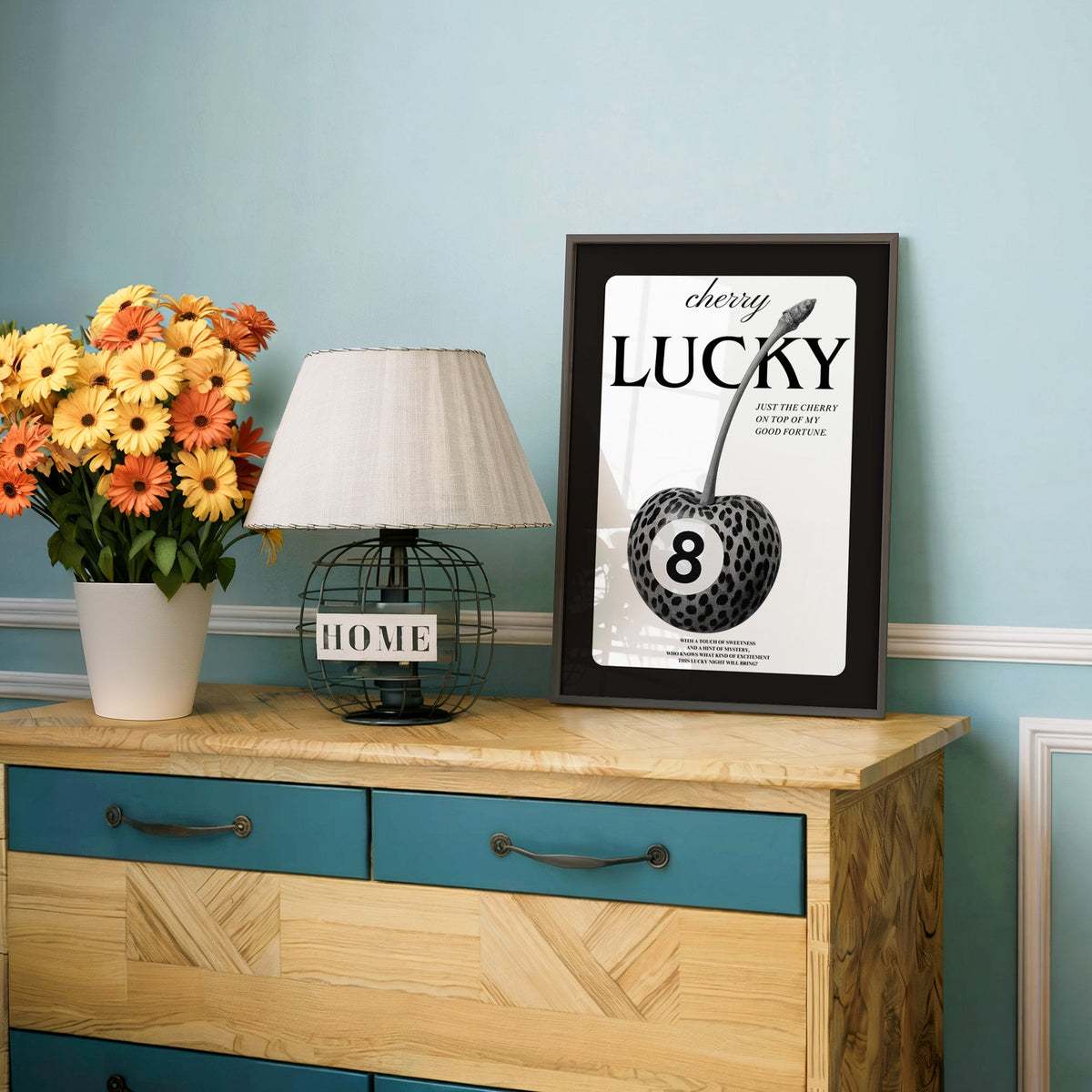 Leopard spotted cherry with eight ball label print in a charcoal frame on a teal dresser beside orange daisies