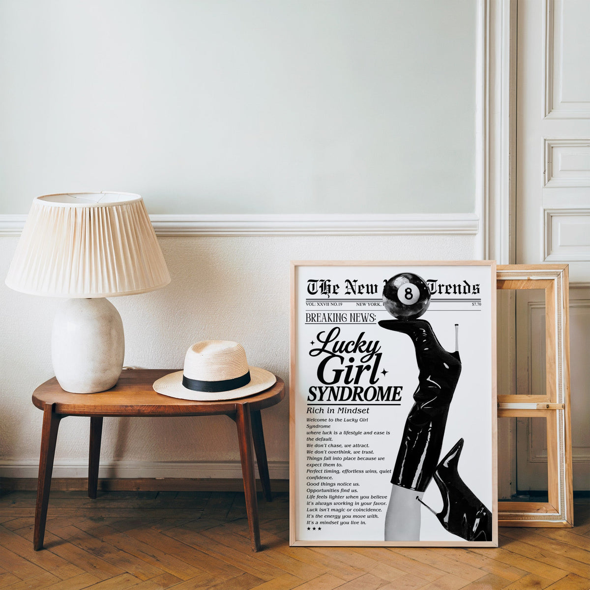 Lucky Girl Syndrome mock newspaper with boots print in a pine frame on a wood floor beside a lamp and straw hat