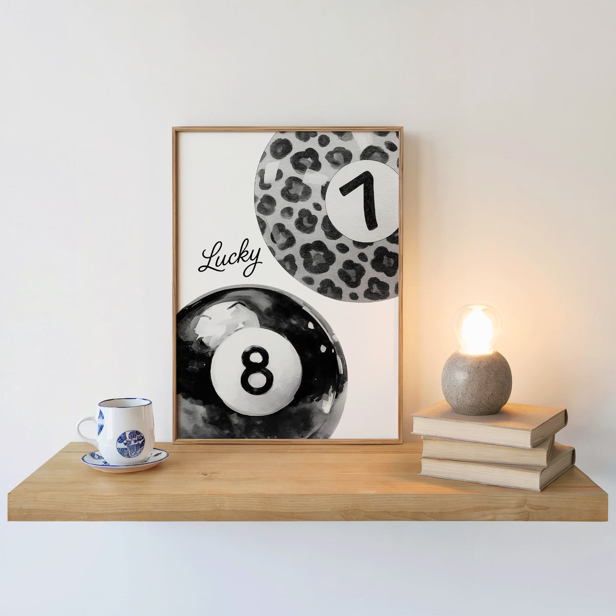 Leopard seven ball and black eight ball watercolor print in an oak frame on a floating shelf beside a glowing lamp