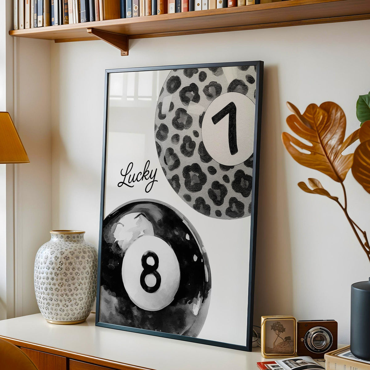 Leopard seven ball and black eight ball watercolor print in a black frame on a console under a bookshelf