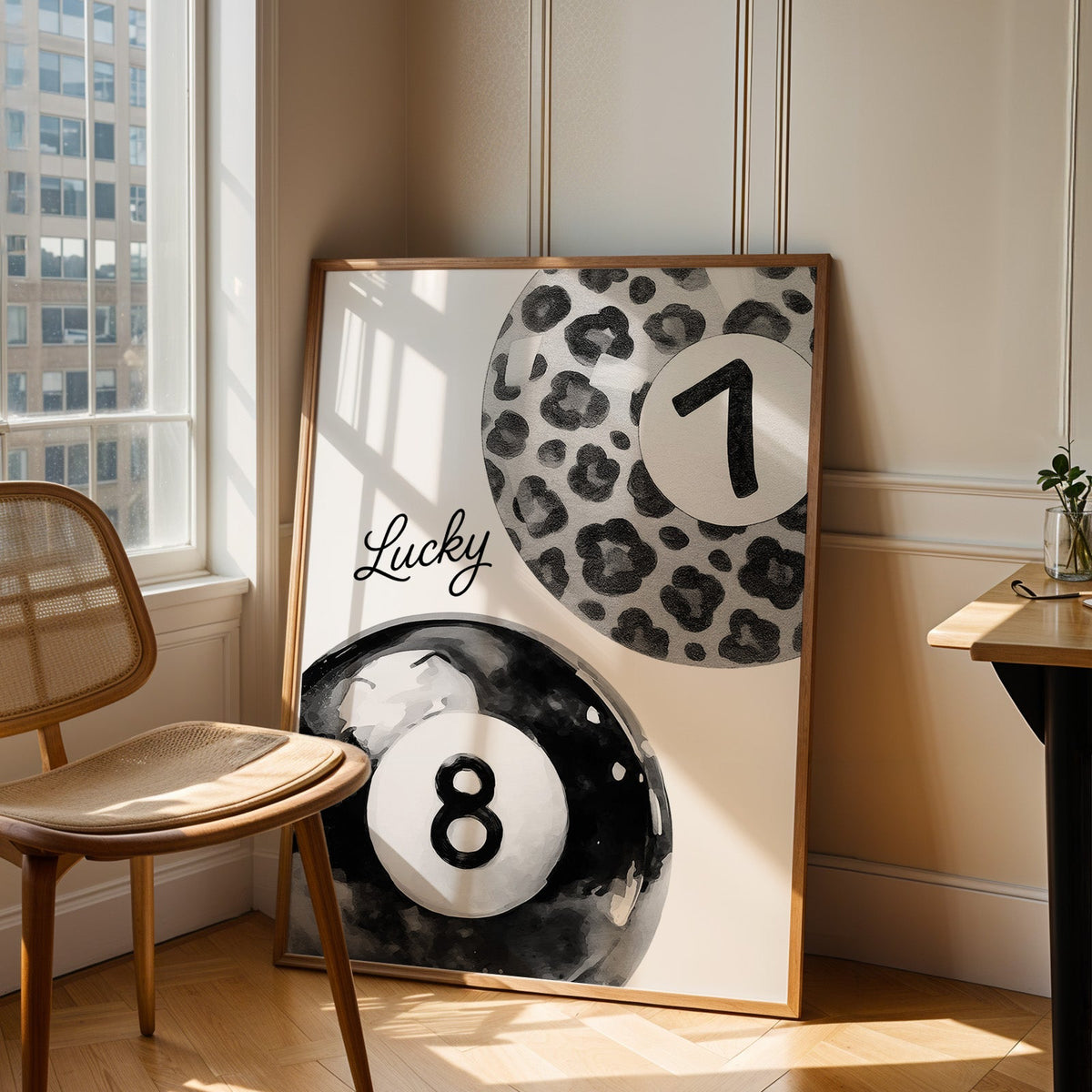 Leopard seven ball and black eight ball watercolor print in an oak frame leaning in a sunlit corner beside a cane chair